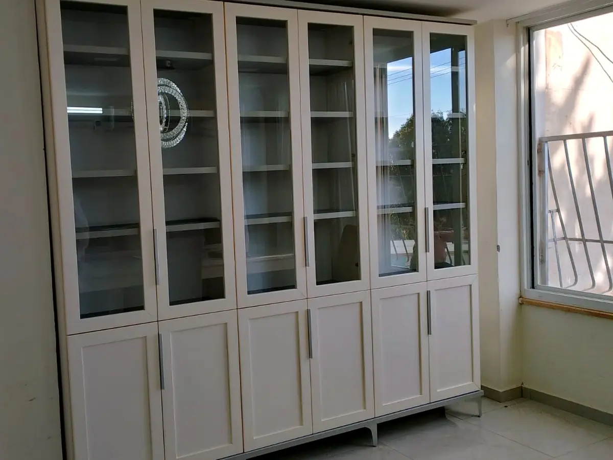 ספרייה רחבה בגוון שמנת עם שש דלתות זכוכית ורגלי מתכת, בסלון מול חלון