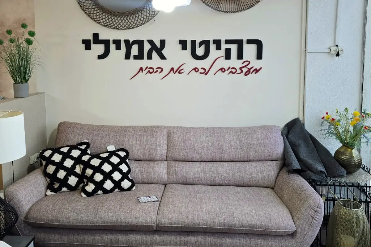 ספה תלת-מושבית בגוון ורוד עתיק, מתחת לשלט של רהיטי אמילי על קיר אולם התצוגה