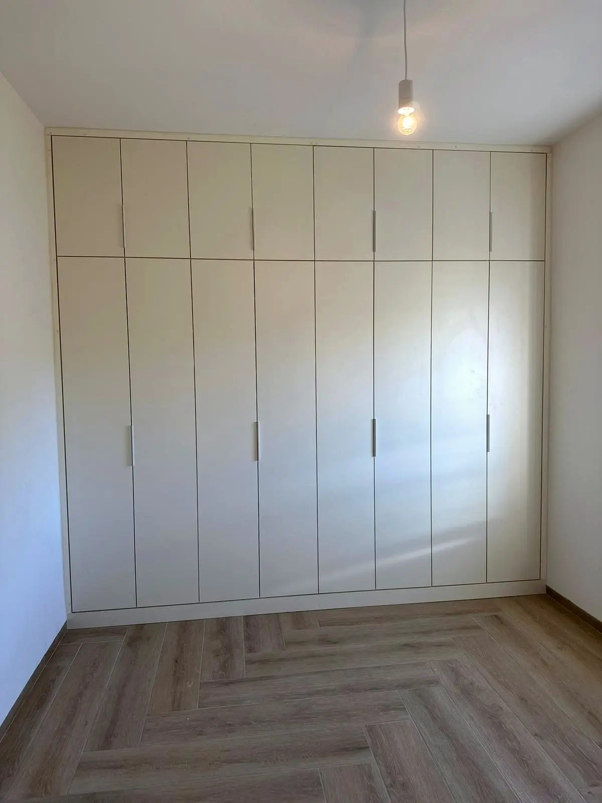 ארון קיר בגוון שמנת עם תאי אחסון עליונים, מותקן מקיר לקיר